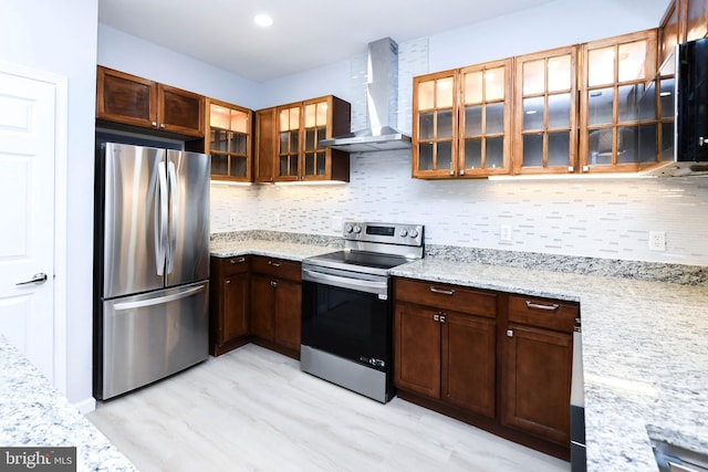 kitchen featuring wall chimney range hood, decorative backsplash, light wood-type flooring, light stone countertops, and stainless steel appliances