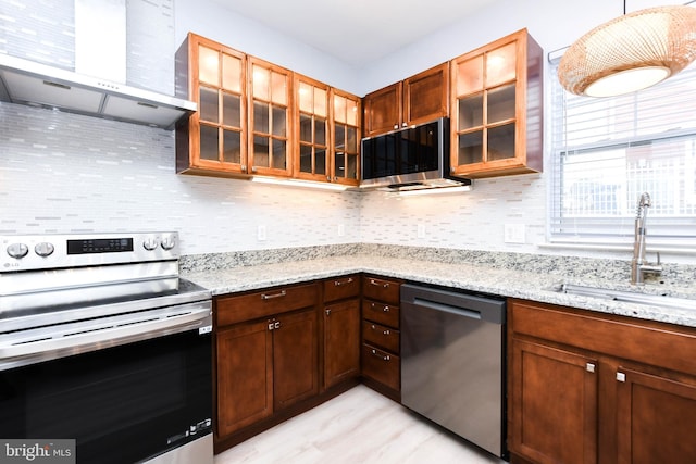 kitchen featuring appliances with stainless steel finishes, wall chimney range hood, decorative light fixtures, light stone countertops, and sink