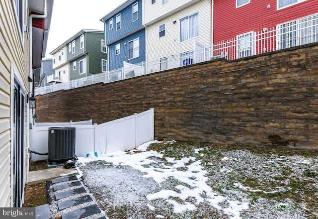 snowy yard featuring fence, a residential view, and central air condition unit