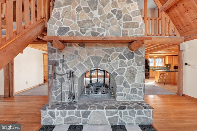 room details featuring black refrigerator, wood-type flooring, a stone fireplace, and beamed ceiling