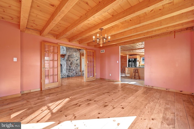 unfurnished living room featuring beam ceiling, french doors, a notable chandelier, and wood-type flooring