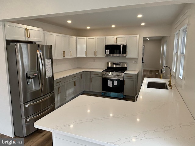 kitchen featuring kitchen peninsula, stainless steel appliances, gray cabinetry, light stone countertops, and sink