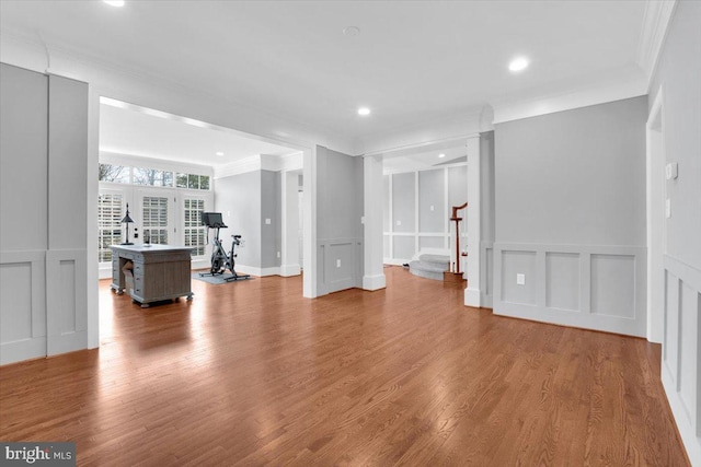 unfurnished living room featuring a decorative wall, ornamental molding, stairs, and wood finished floors