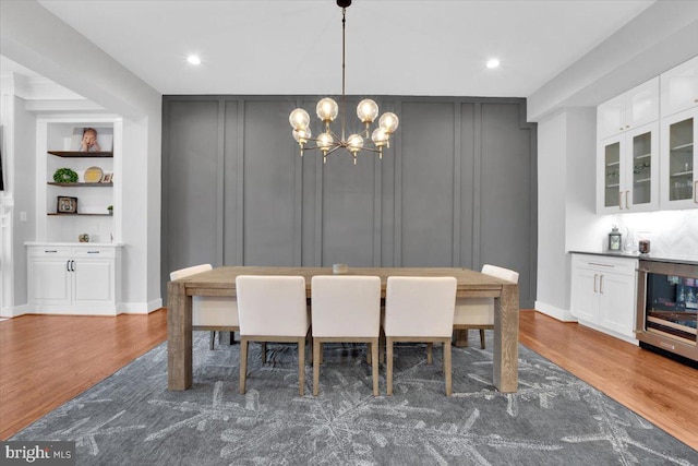 dining space featuring built in features, an inviting chandelier, wood finished floors, and a decorative wall