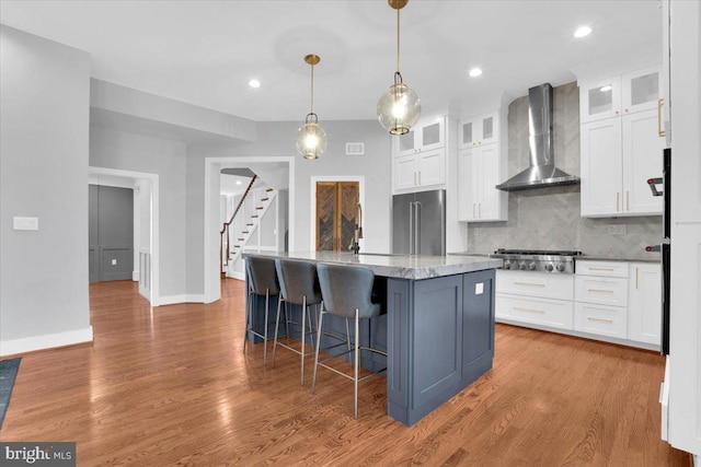 kitchen featuring white cabinets, wall chimney exhaust hood, light wood-style flooring, and stainless steel appliances