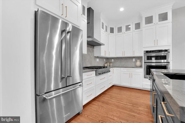 kitchen with tasteful backsplash, stainless steel appliances, wall chimney exhaust hood, white cabinets, and light stone countertops