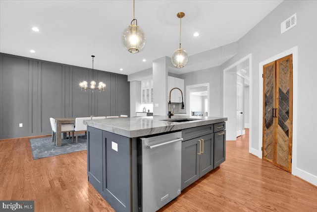 kitchen featuring visible vents, gray cabinetry, a sink, stainless steel dishwasher, and a decorative wall