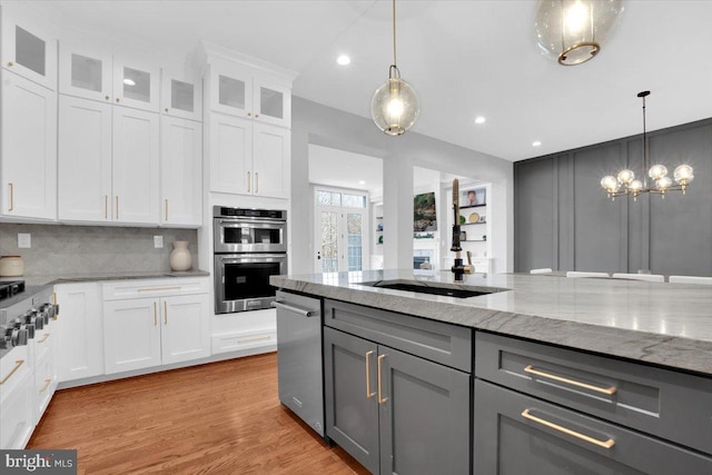 kitchen featuring light stone countertops, gray cabinets, stainless steel appliances, glass insert cabinets, and tasteful backsplash