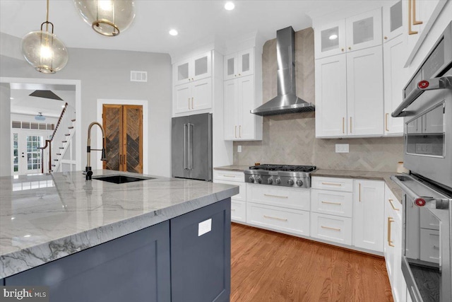 kitchen with light wood finished floors, visible vents, wall chimney range hood, stainless steel appliances, and a sink