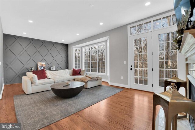 living room with an accent wall, recessed lighting, wood finished floors, and baseboards