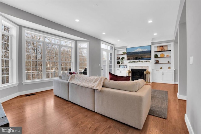 living area featuring wood finished floors, baseboards, visible vents, a premium fireplace, and recessed lighting