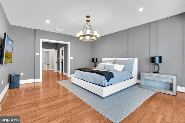 bedroom featuring light wood finished floors, visible vents, recessed lighting, an inviting chandelier, and a decorative wall