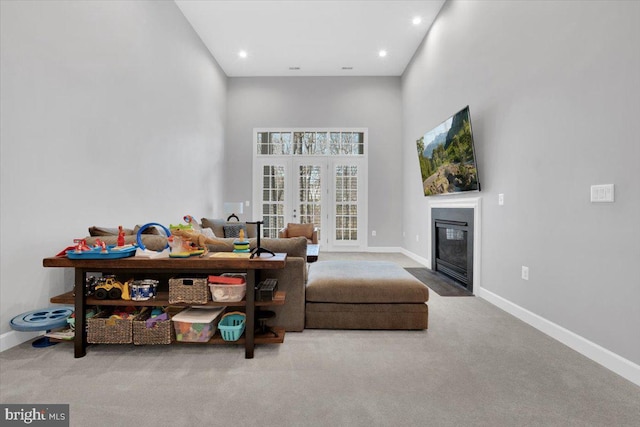 living area with a fireplace with flush hearth, french doors, baseboards, and carpet