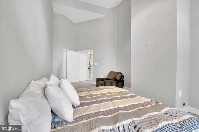 carpeted bedroom with a high ceiling and baseboards