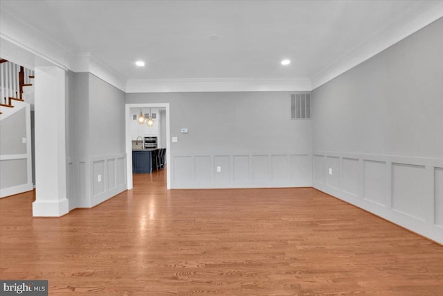 unfurnished room featuring visible vents, ornamental molding, light wood-style floors, a decorative wall, and stairs