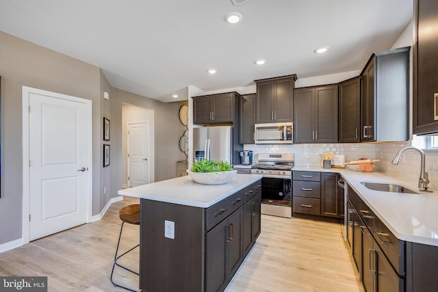 kitchen with light hardwood / wood-style floors, a center island, a breakfast bar, sink, and appliances with stainless steel finishes