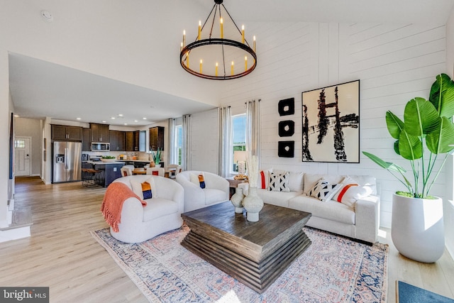 living room featuring wood walls, a chandelier, light hardwood / wood-style flooring, and a high ceiling