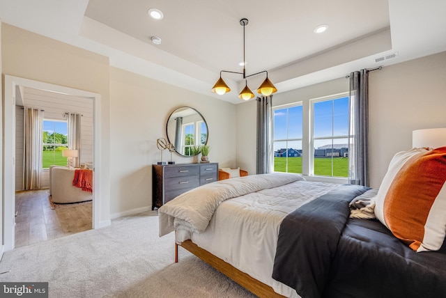 bedroom with a raised ceiling, a chandelier, light wood-type flooring, and multiple windows