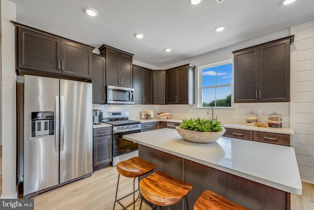 kitchen featuring appliances with stainless steel finishes, decorative backsplash, a kitchen breakfast bar, dark brown cabinets, and light hardwood / wood-style flooring