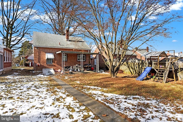 snow covered back of property featuring a playground