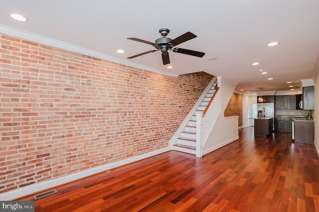 unfurnished living room featuring sink, ornamental molding, dark hardwood / wood-style floors, and brick wall