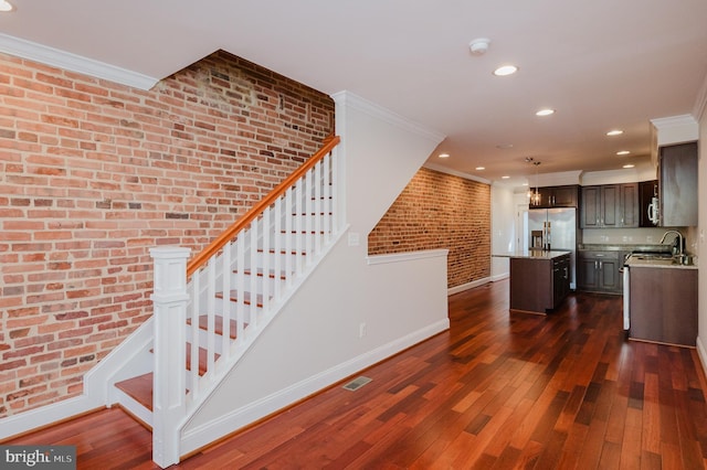 kitchen featuring dark wood-type flooring, dark brown cabinets, a center island, and brick wall