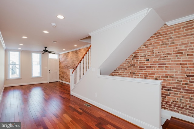 foyer entrance with dark hardwood / wood-style flooring, crown molding, ceiling fan, and brick wall