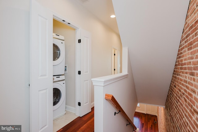 laundry room featuring brick wall, stacked washer / dryer, and dark hardwood / wood-style flooring