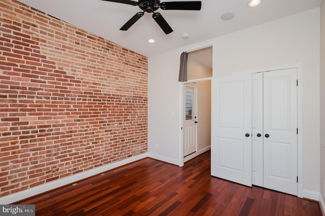 unfurnished bedroom featuring ceiling fan, brick wall, dark hardwood / wood-style floors, and a closet