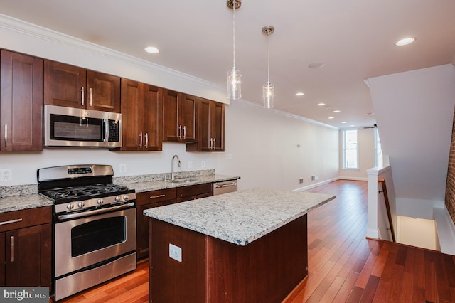 kitchen with sink, crown molding, decorative light fixtures, appliances with stainless steel finishes, and a kitchen island