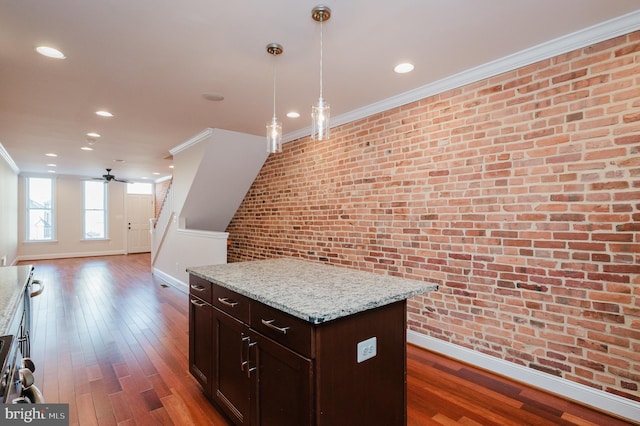 kitchen featuring hanging light fixtures, crown molding, brick wall, and light stone counters