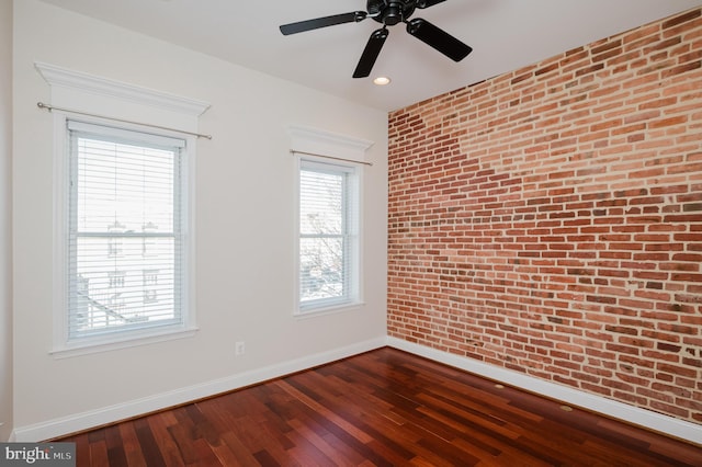 empty room with ceiling fan, brick wall, and wood-type flooring