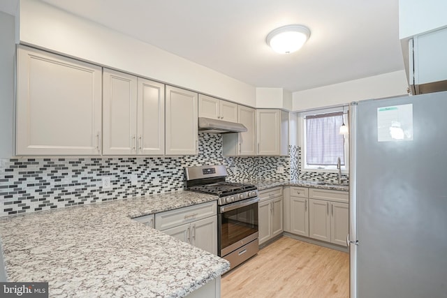 kitchen with stainless steel appliances, tasteful backsplash, sink, light stone counters, and gray cabinetry