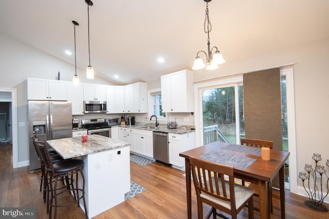 kitchen featuring appliances with stainless steel finishes, a center island, light stone counters, white cabinets, and decorative light fixtures