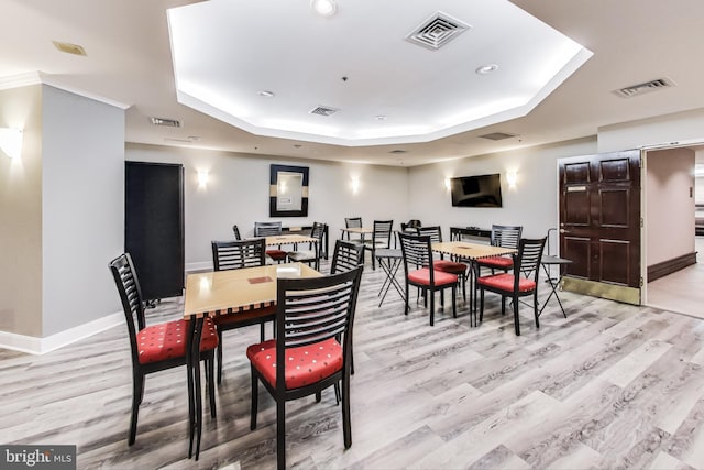 dining area featuring a tray ceiling, ornamental molding, and light hardwood / wood-style flooring