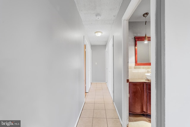 corridor featuring light tile patterned floors, a textured ceiling, a sink, and baseboards