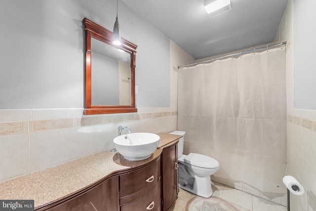 bathroom with a wainscoted wall, tile walls, toilet, vanity, and tile patterned flooring