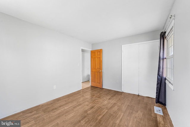 unfurnished bedroom featuring a closet, visible vents, and wood finished floors