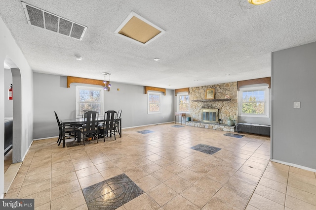 dining area with a textured ceiling, a fireplace, visible vents, baseboards, and tile patterned floors