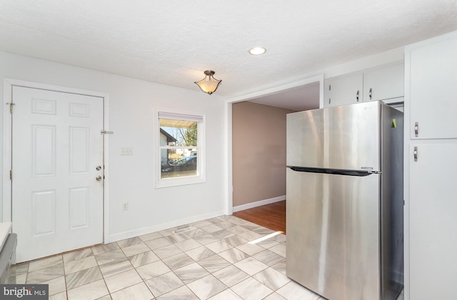 kitchen featuring white cabinetry, baseboards, freestanding refrigerator, and a textured ceiling