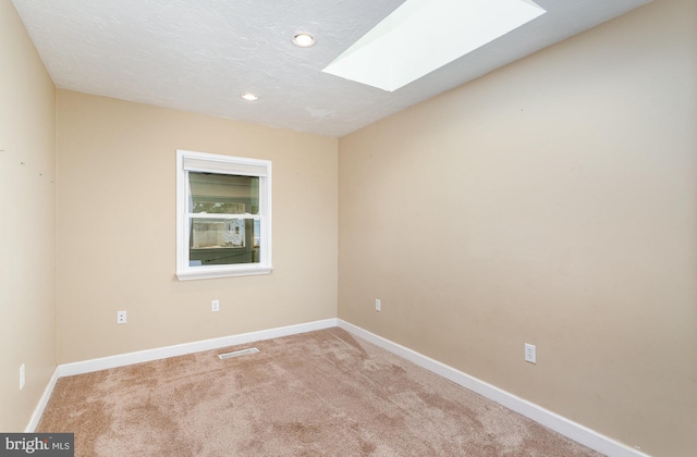 carpeted empty room with visible vents, a textured ceiling, a skylight, and baseboards