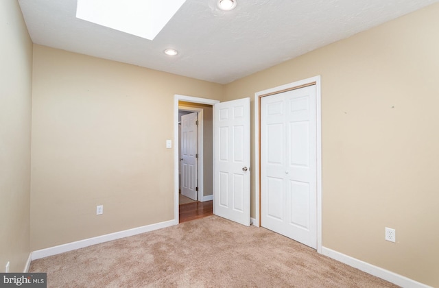 unfurnished bedroom with baseboards, light colored carpet, recessed lighting, a skylight, and a closet