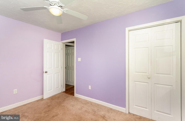 unfurnished bedroom featuring baseboards, light carpet, a textured ceiling, and a closet