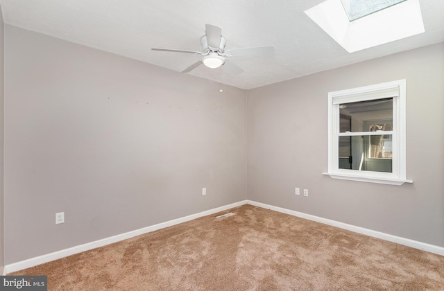 unfurnished room with visible vents, a ceiling fan, a skylight, carpet flooring, and baseboards