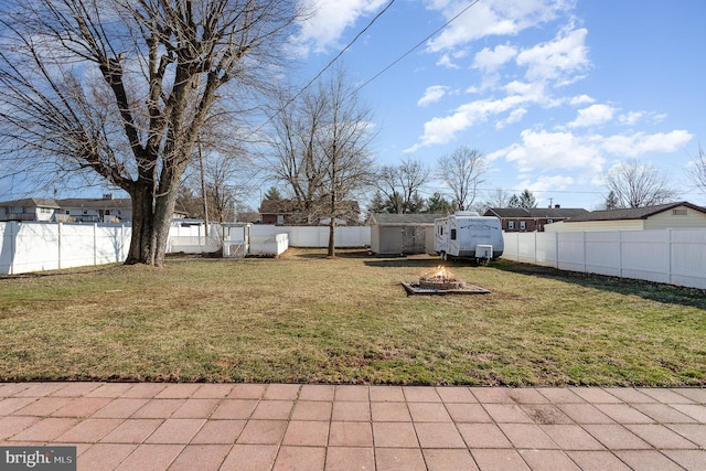 view of yard with a storage unit, an outbuilding, a fenced backyard, and an outdoor fire pit