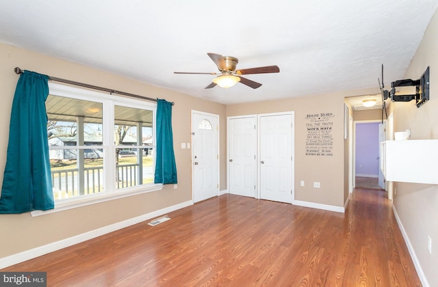 interior space featuring ceiling fan, visible vents, baseboards, and wood finished floors