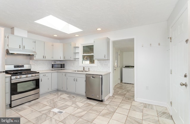 kitchen featuring under cabinet range hood, light countertops, washer / dryer, appliances with stainless steel finishes, and a sink