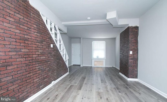 interior space with brick wall, light hardwood / wood-style flooring, and beam ceiling