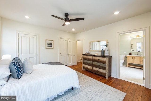 bedroom featuring ceiling fan, ensuite bathroom, sink, multiple closets, and dark hardwood / wood-style flooring