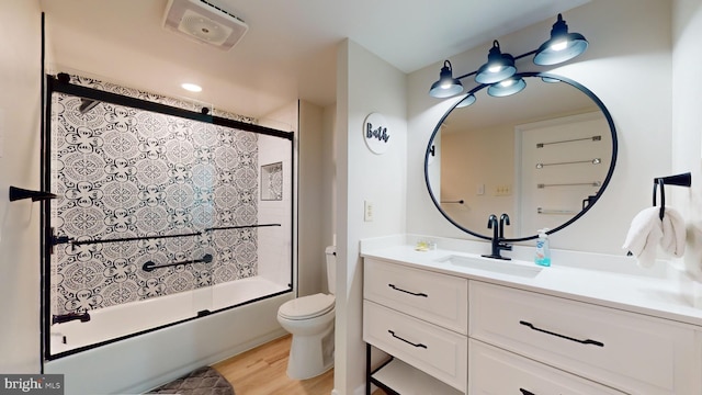 full bathroom featuring wood-type flooring, enclosed tub / shower combo, vanity, and toilet